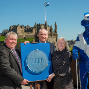 Richard Lochhead, Malcolm Roughead, Barbara Smith hold LEED plaque outside Johnnie Walker Princes Street